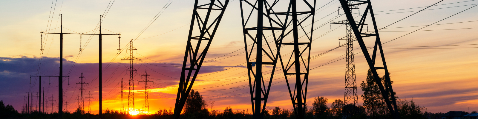 Silhouetted power lines and pylons stretch across a vibrant sunset sky with orange and purple hues.