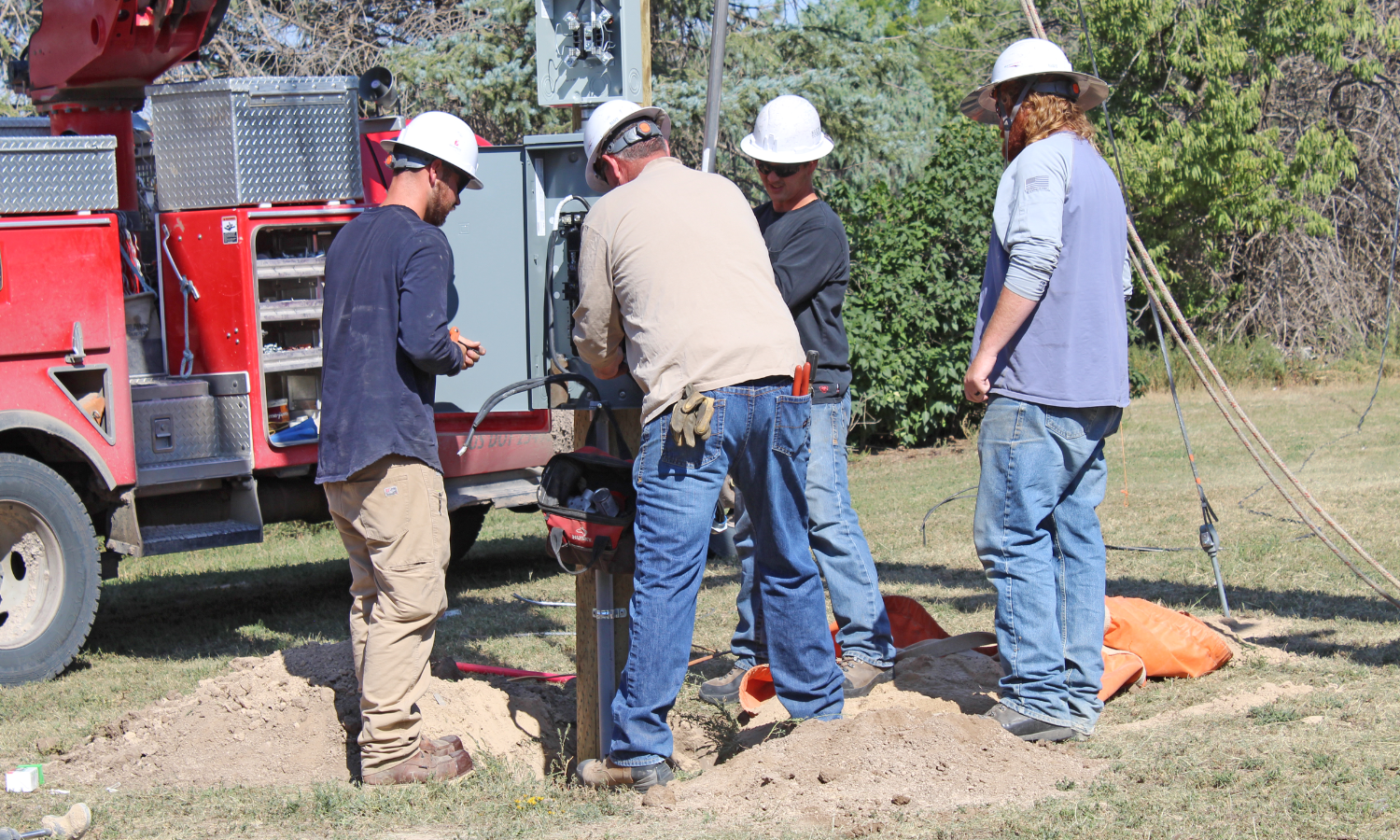 High West Energy line crew working on electrical equipment and underground service connections beside a utility truck during a field construction project.