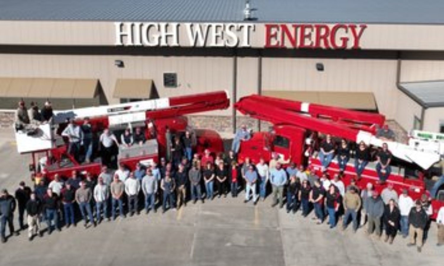 Group photo of High West Energy employees and utility trucks gathered outside the High West Energy headquarters building.