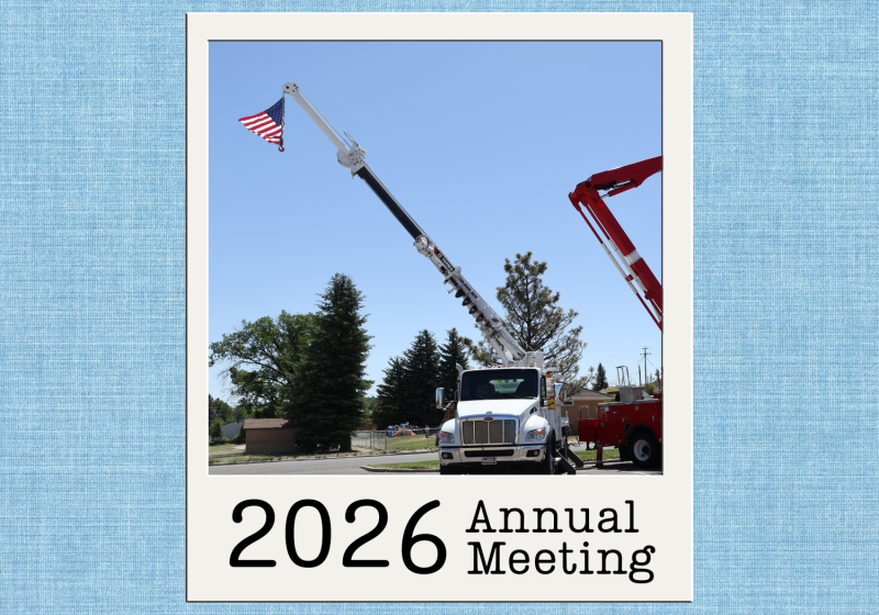 Bucket truck displaying an American flag during the 2026 High West Energy Annual Meeting, with utility equipment and boom arms extended against a clear blue sky.