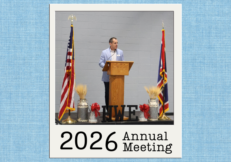 Speaker providing cooperative updates during the 2026 High West Energy Annual Meeting while standing at a podium between American and Wyoming state flags.