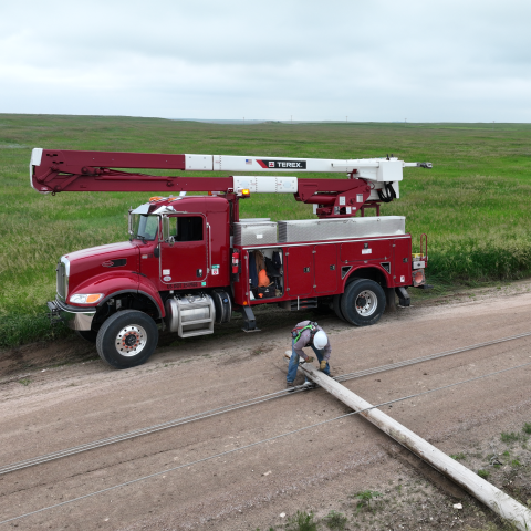 Truck on the side of the road, while worker is fixing the down pole.